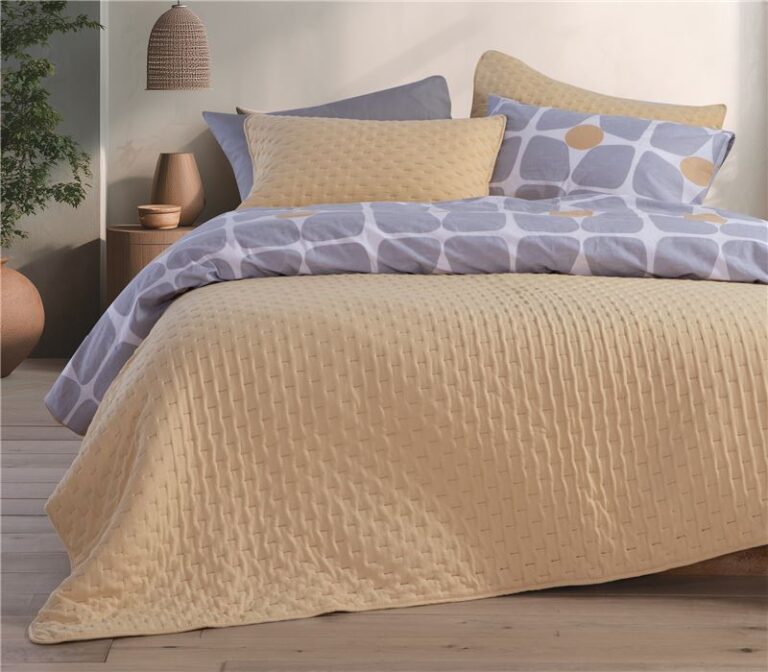 Modern bedroom featuring a beige quilted bedspread layered with geometric-patterned bedding in soft lavender and cream tones, creating a warm and contemporary look.
