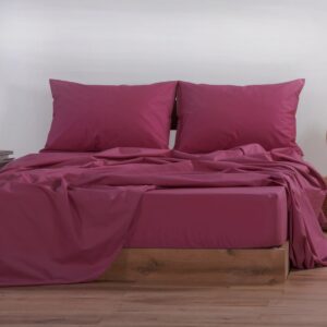Double bed dressed in solid berry pink bedding, featuring matching pillowcases and softly draped sheets on a wooden bed frame in a minimalist bedroom setting.